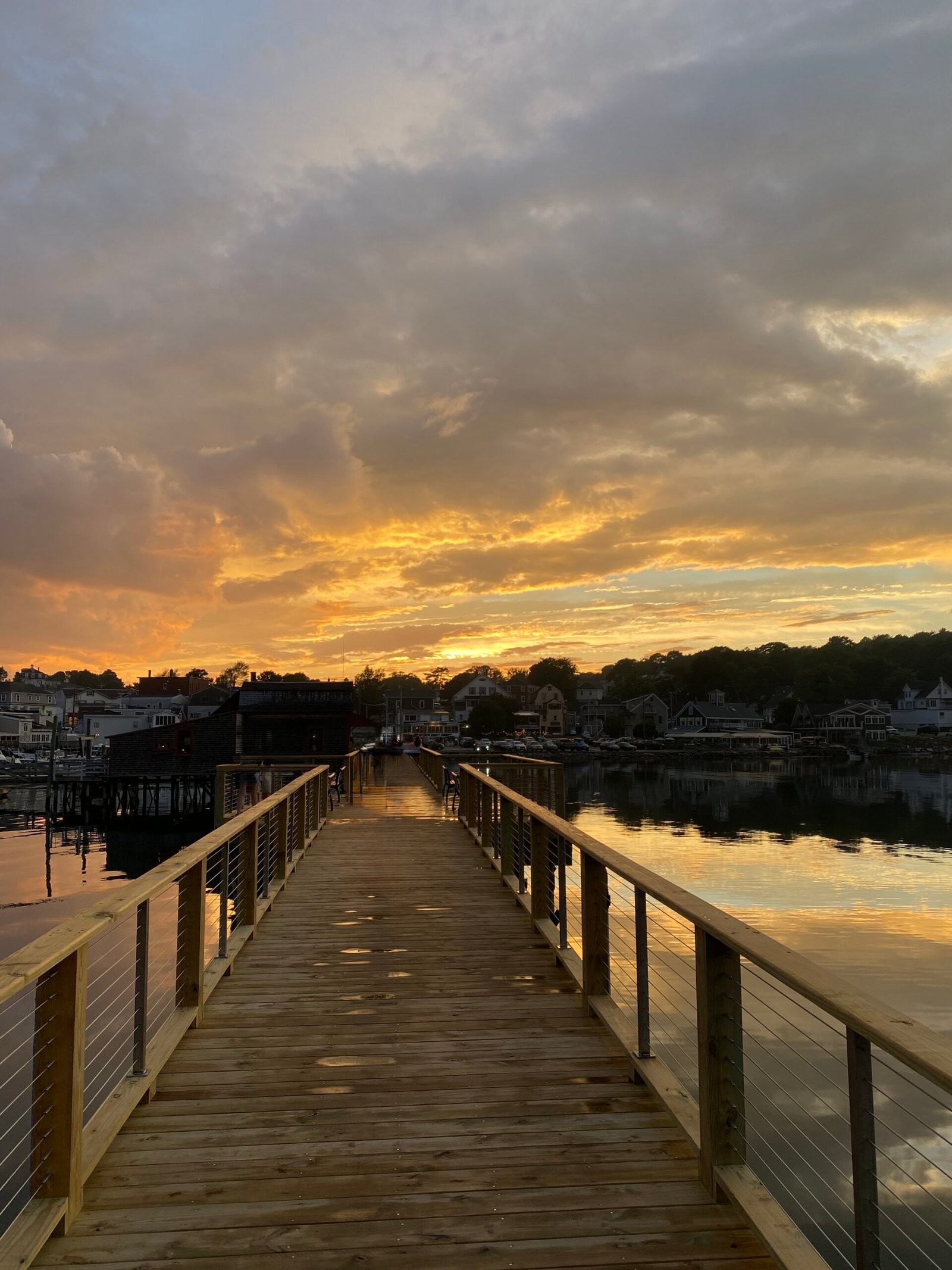 Long wooden pier leading towards a dramatic golden sunset over the water